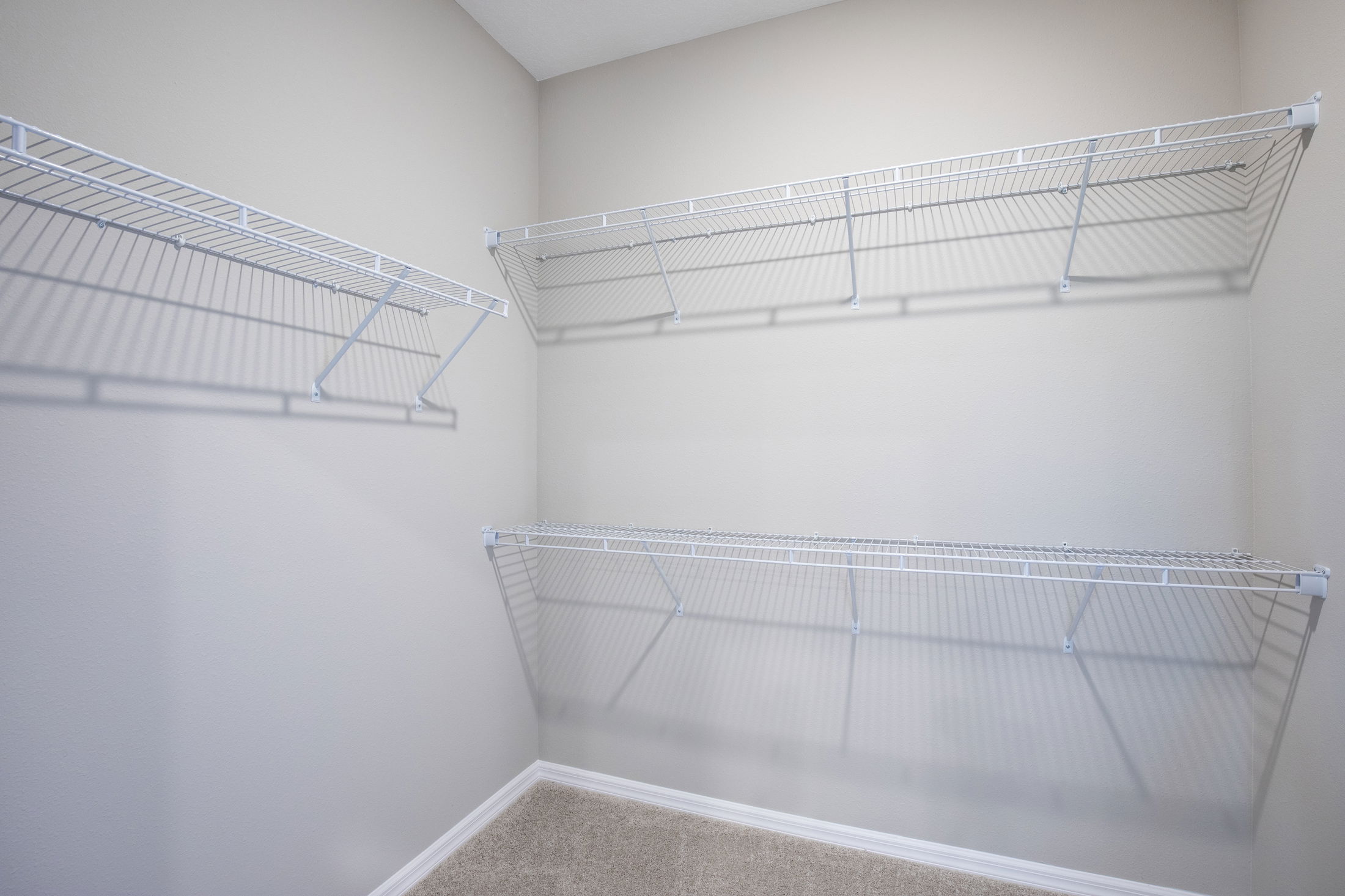 Empty walk-in closet with beige walls and white wire shelving.