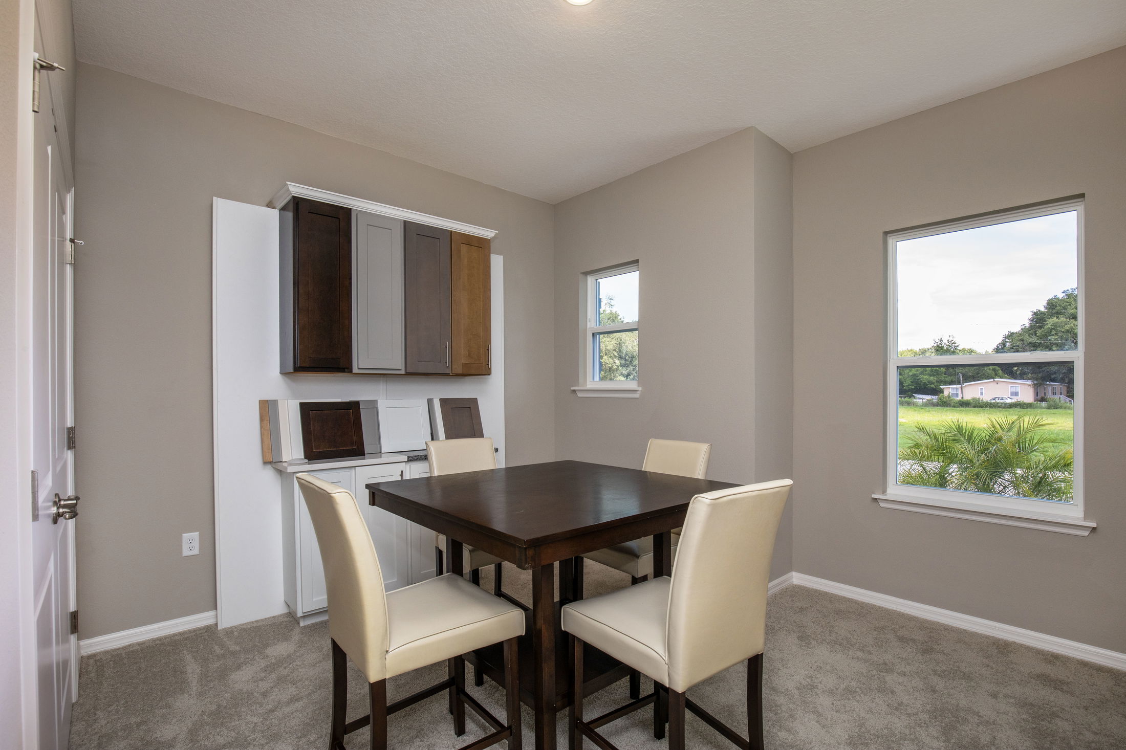Modern dining room with a dark wood table, four cream chairs, and natural light from large windows.