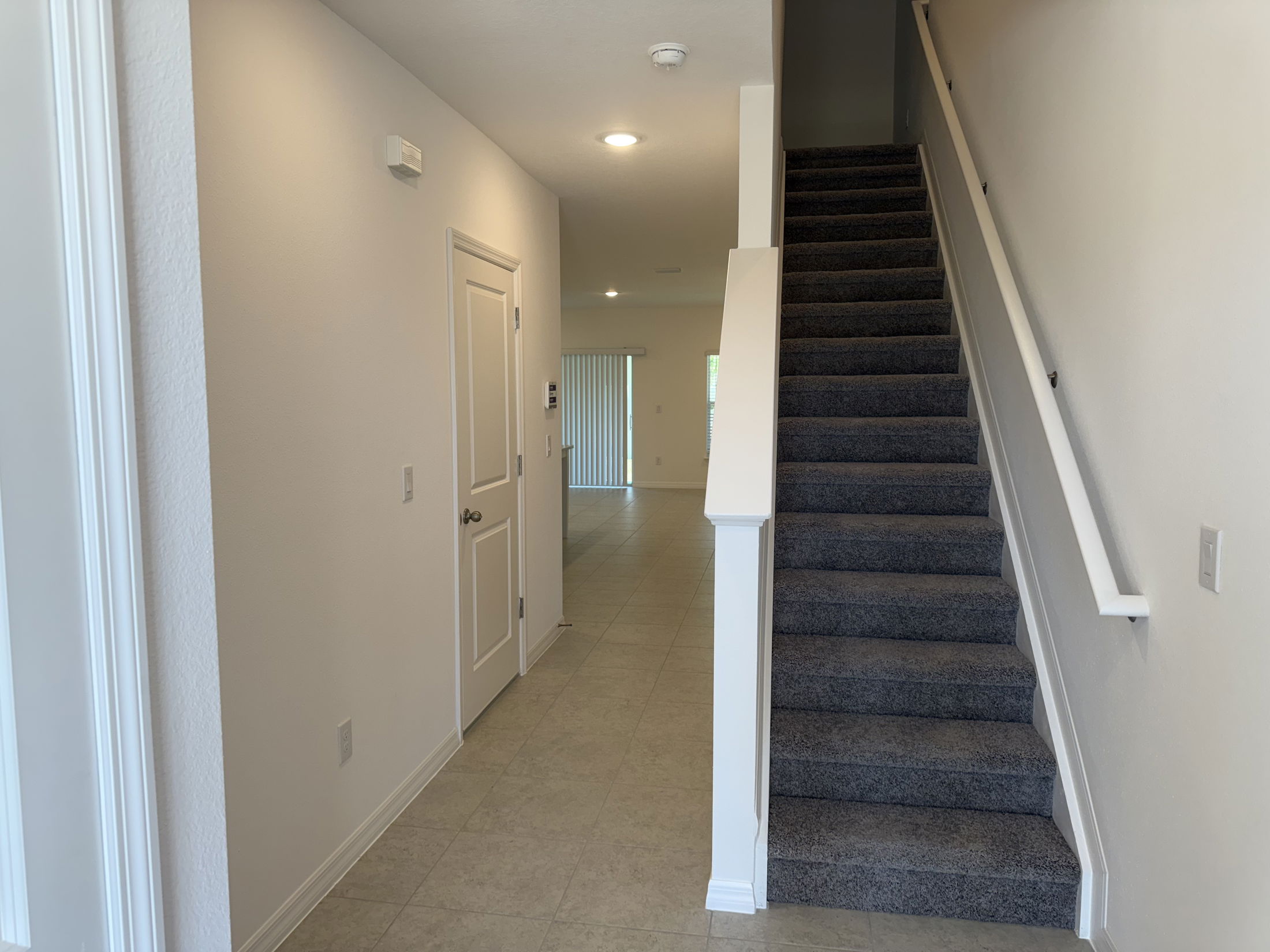 Modern interior hallway with carpeted stairs leading to the upper floor, tiled flooring, and white walls.