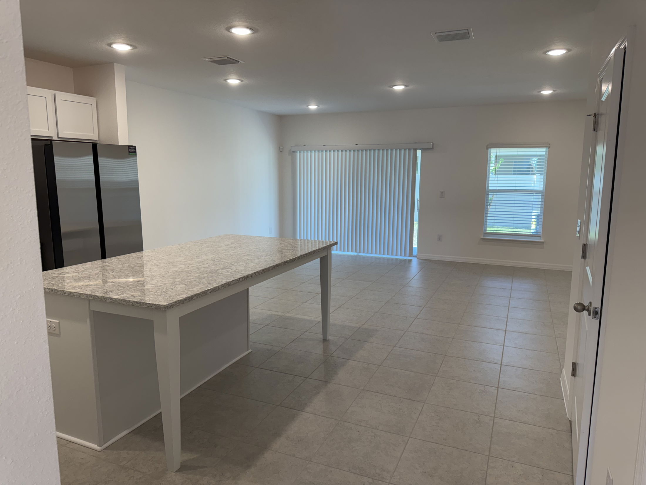 Modern kitchen interior with large granite island, tiled floor, and stainless steel appliances.