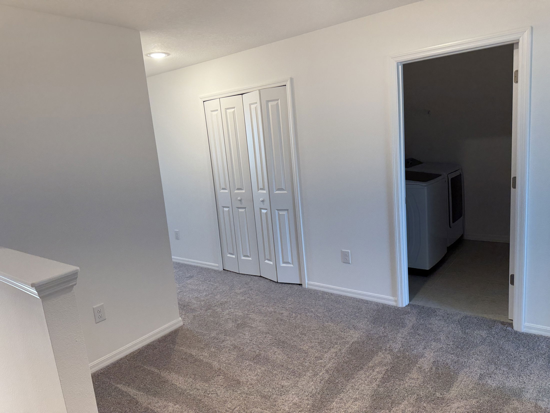 Bright hallway with carpet leads to a laundry room featuring a visible washer and closet doors.