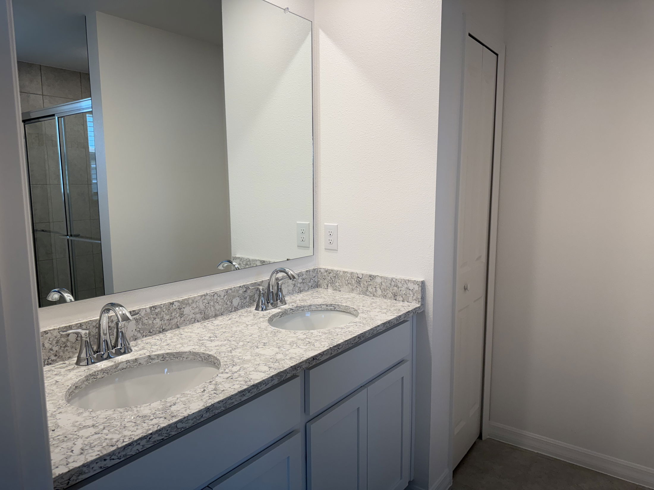 A modern bathroom features a dual-sink vanity with granite countertops, large mirror, and a glass-enclosed shower.