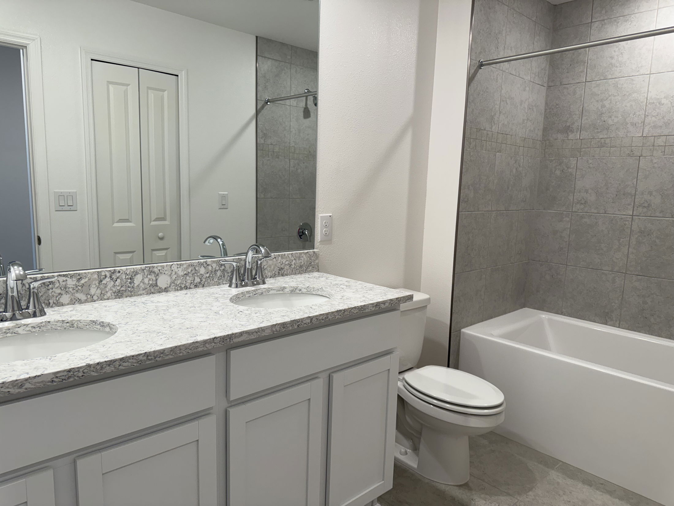 Modern bathroom with dual sinks, marble countertop, and a tiled shower-bathtub combination.
