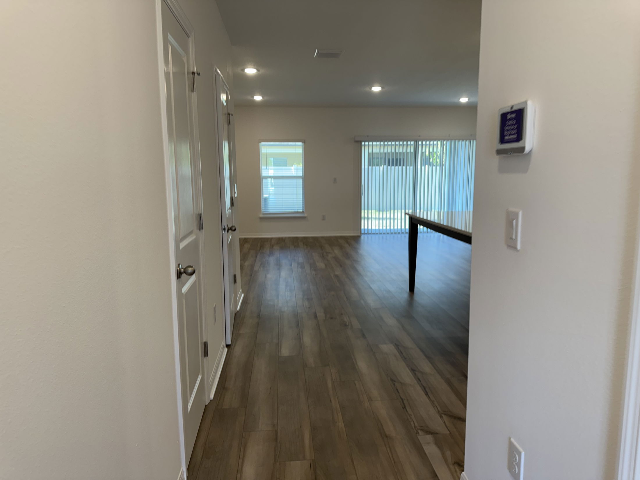 Modern empty room with wood flooring, white walls, and large windows with vertical blinds offering natural light.