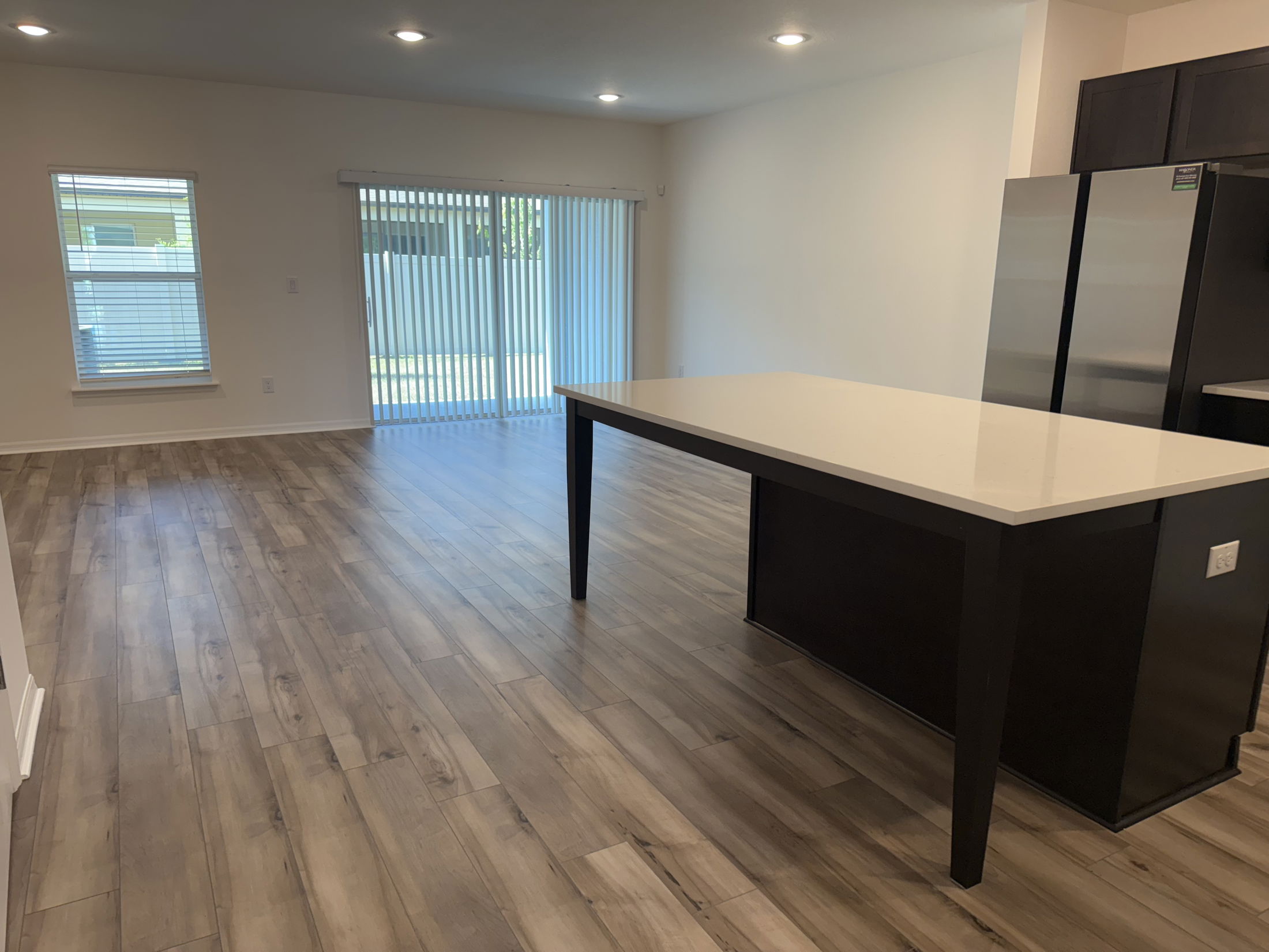 Modern open-plan kitchen and living area with wooden flooring, large windows, and a sleek kitchen island.