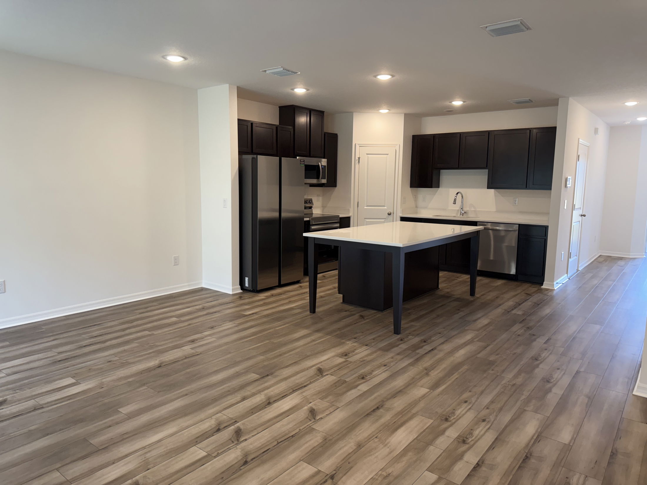 Modern kitchen with dark cabinets, stainless steel appliances, and a spacious island, featuring light wood laminate flooring.