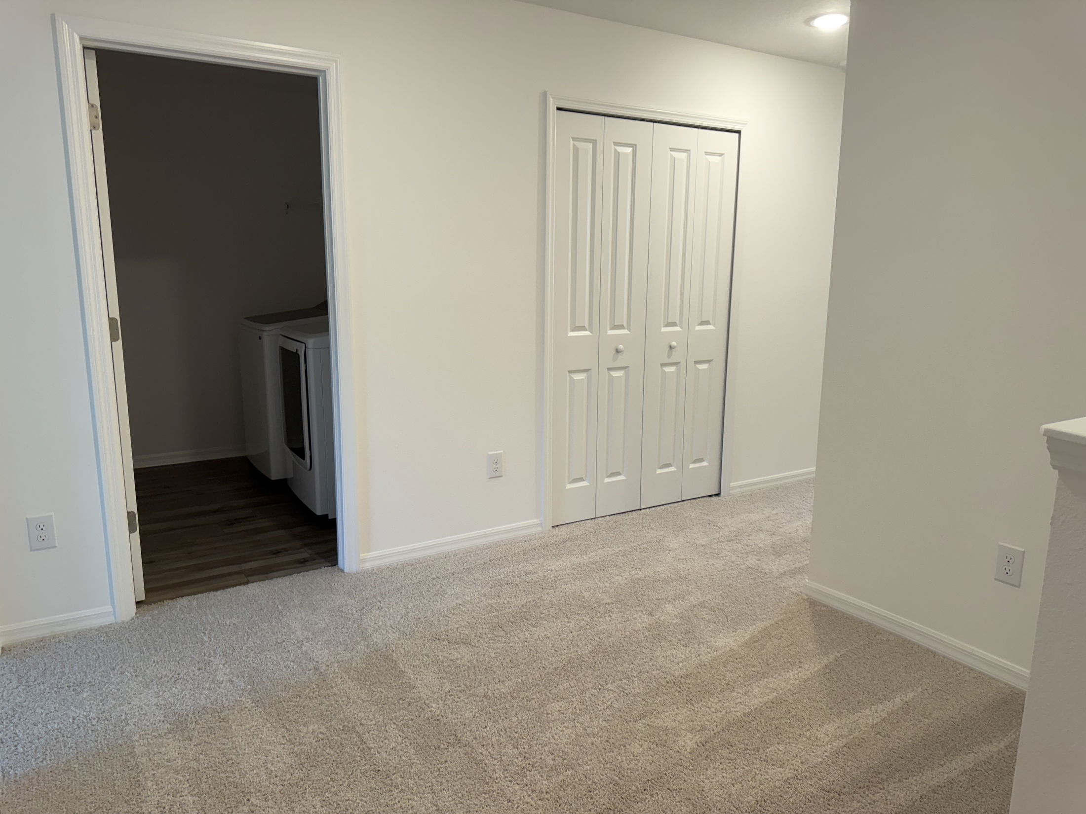 Modern laundry room with washer and dryer adjacent to a carpeted hallway in a new home.