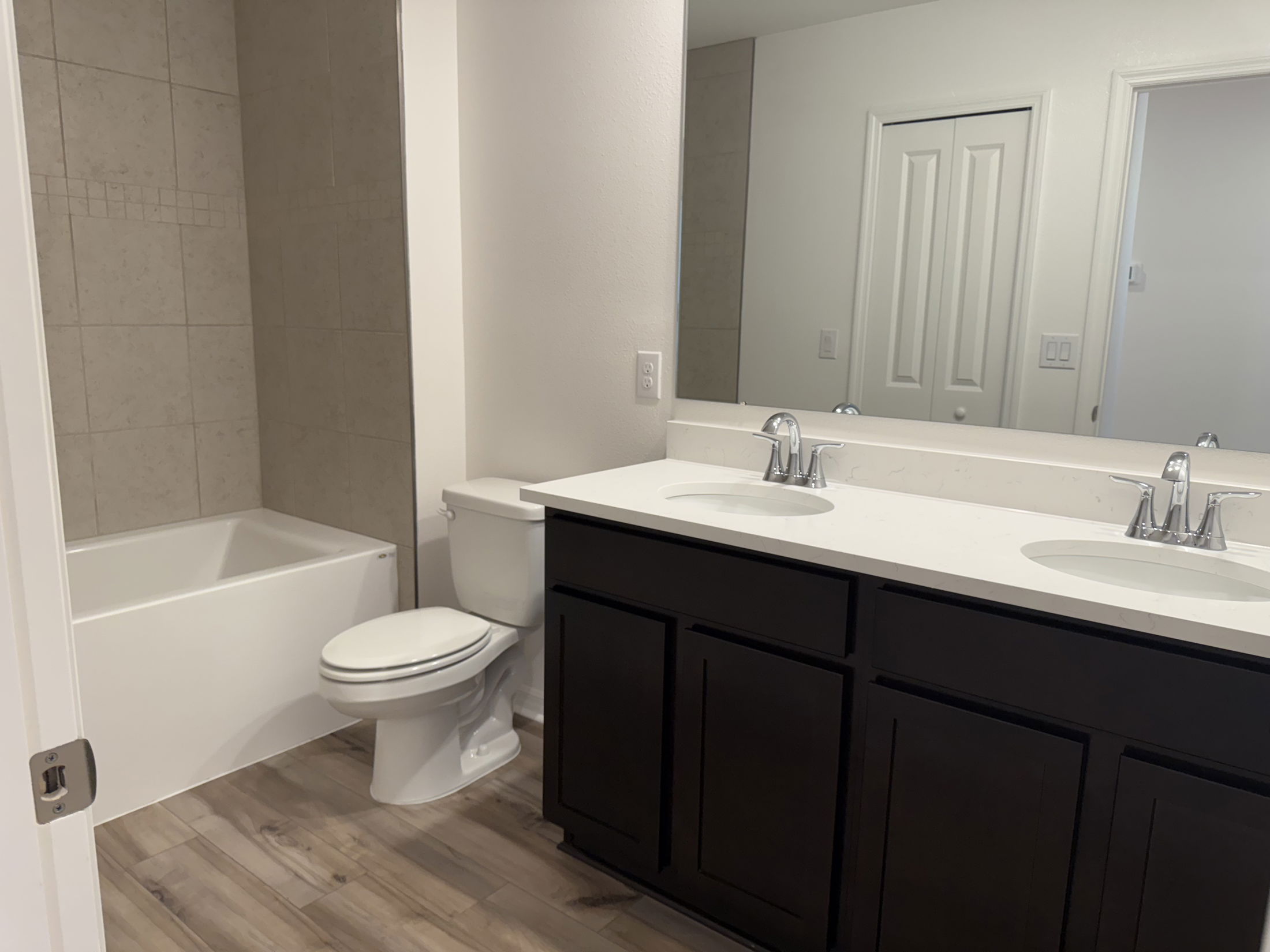 Modern bathroom with dual sinks, bathtub, toilet, and dark wood cabinetry.