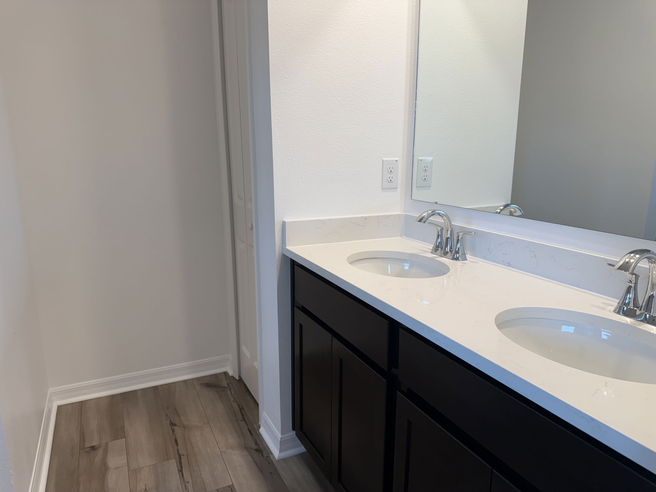 Modern bathroom with double sink vanity, white countertop, and wooden floor.