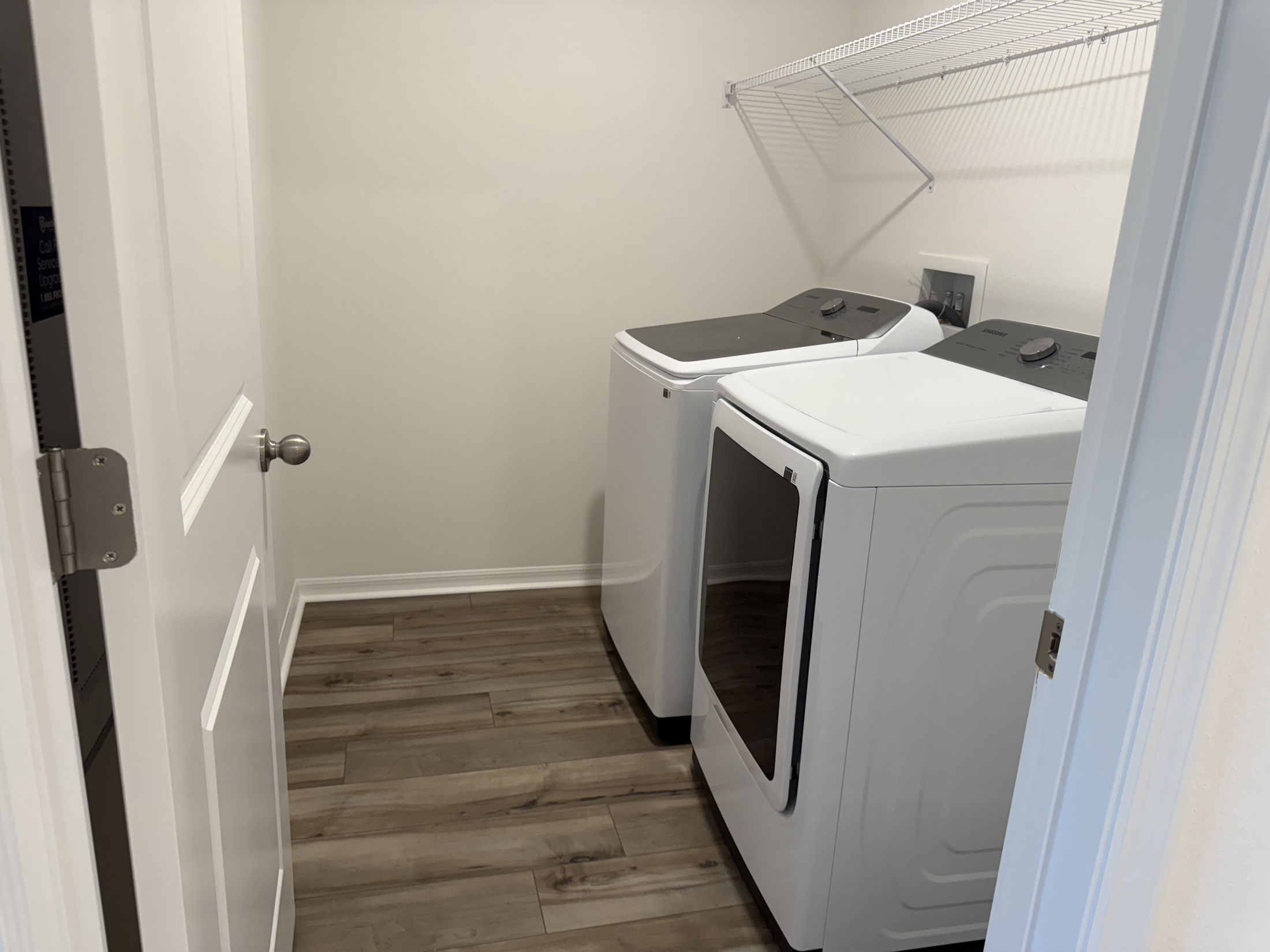 Laundry room with modern washer and dryer on hardwood floor and a wire shelf above.