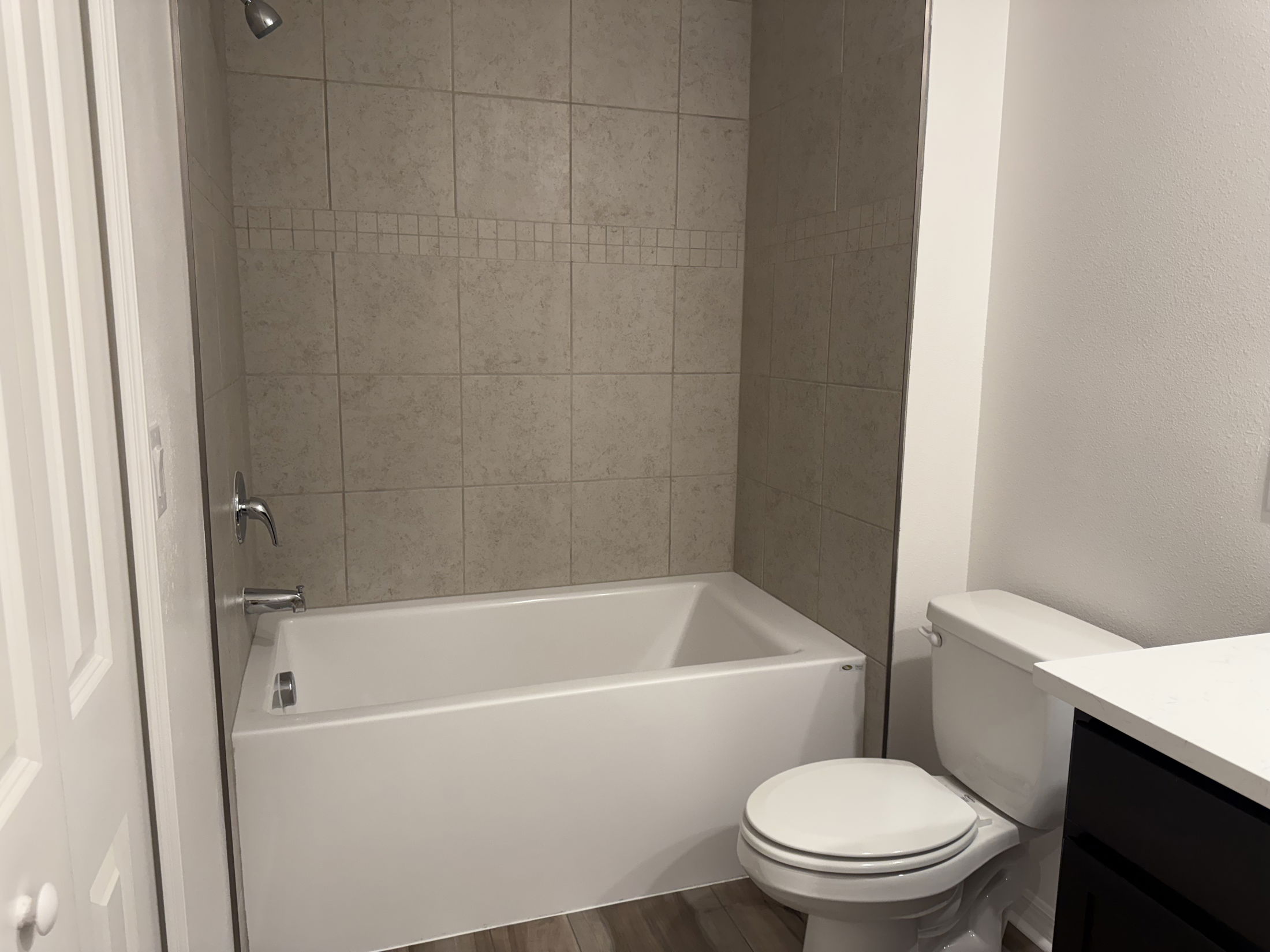 Modern bathroom with a white bathtub, tiled walls, toilet, and dark vanity cabinet.