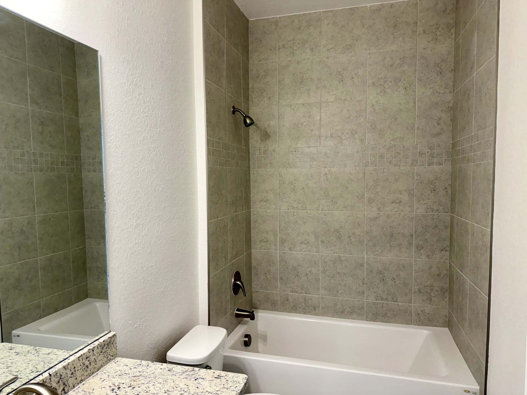 Modern bathroom with a granite countertop, tiled bathtub, and a wall-mounted showerhead.