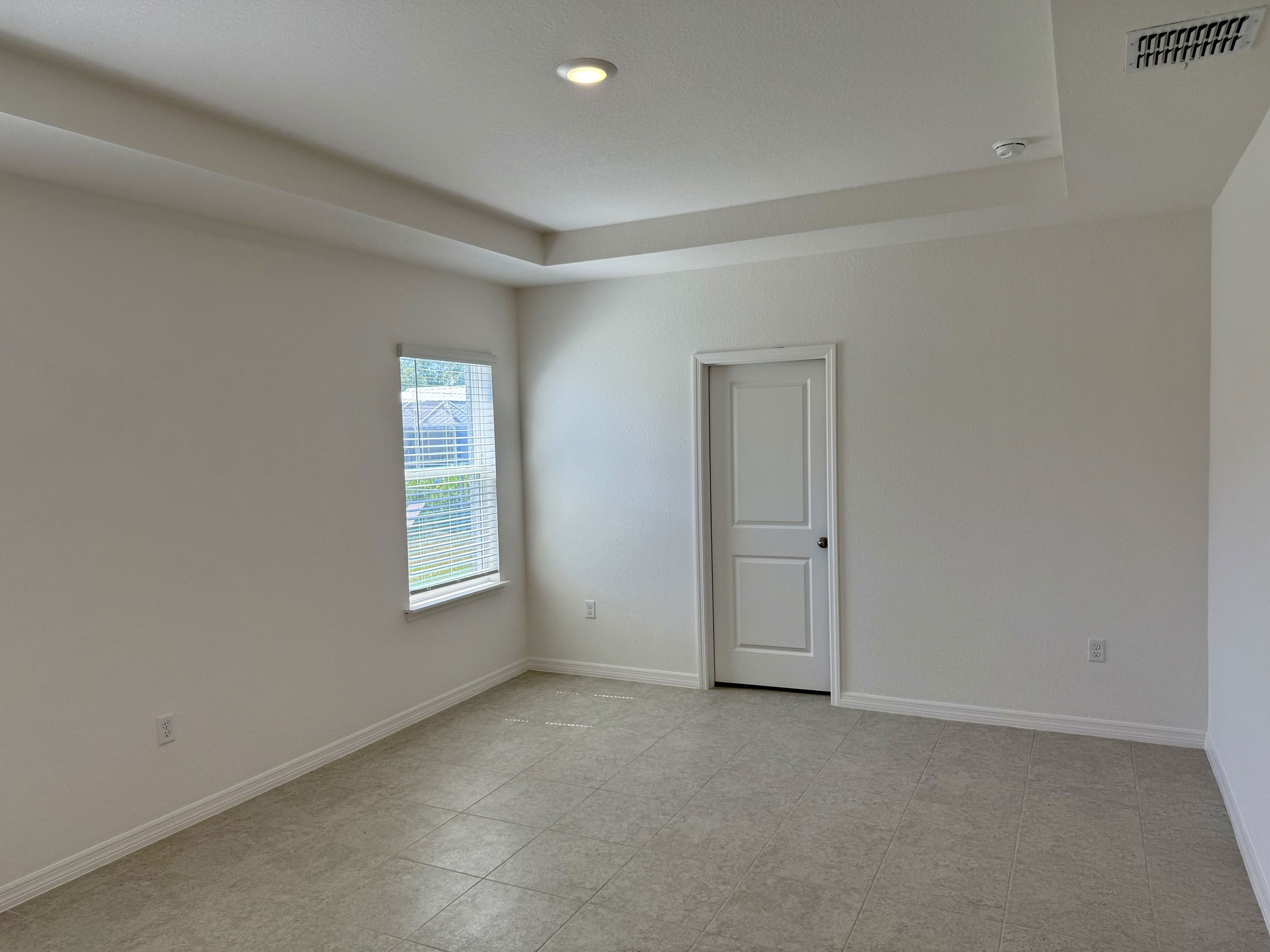 Empty room with a window and white walls featuring a tiled floor and a closed door.