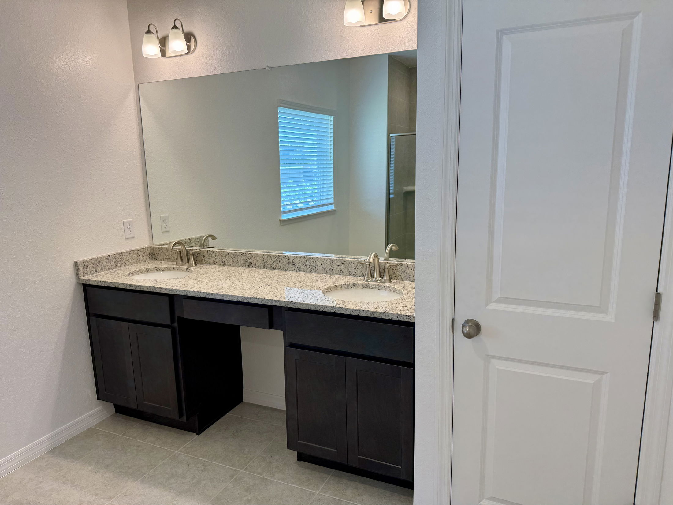 Modern bathroom with a dual-sink granite countertop vanity, large mirror, and elegant light fixtures.