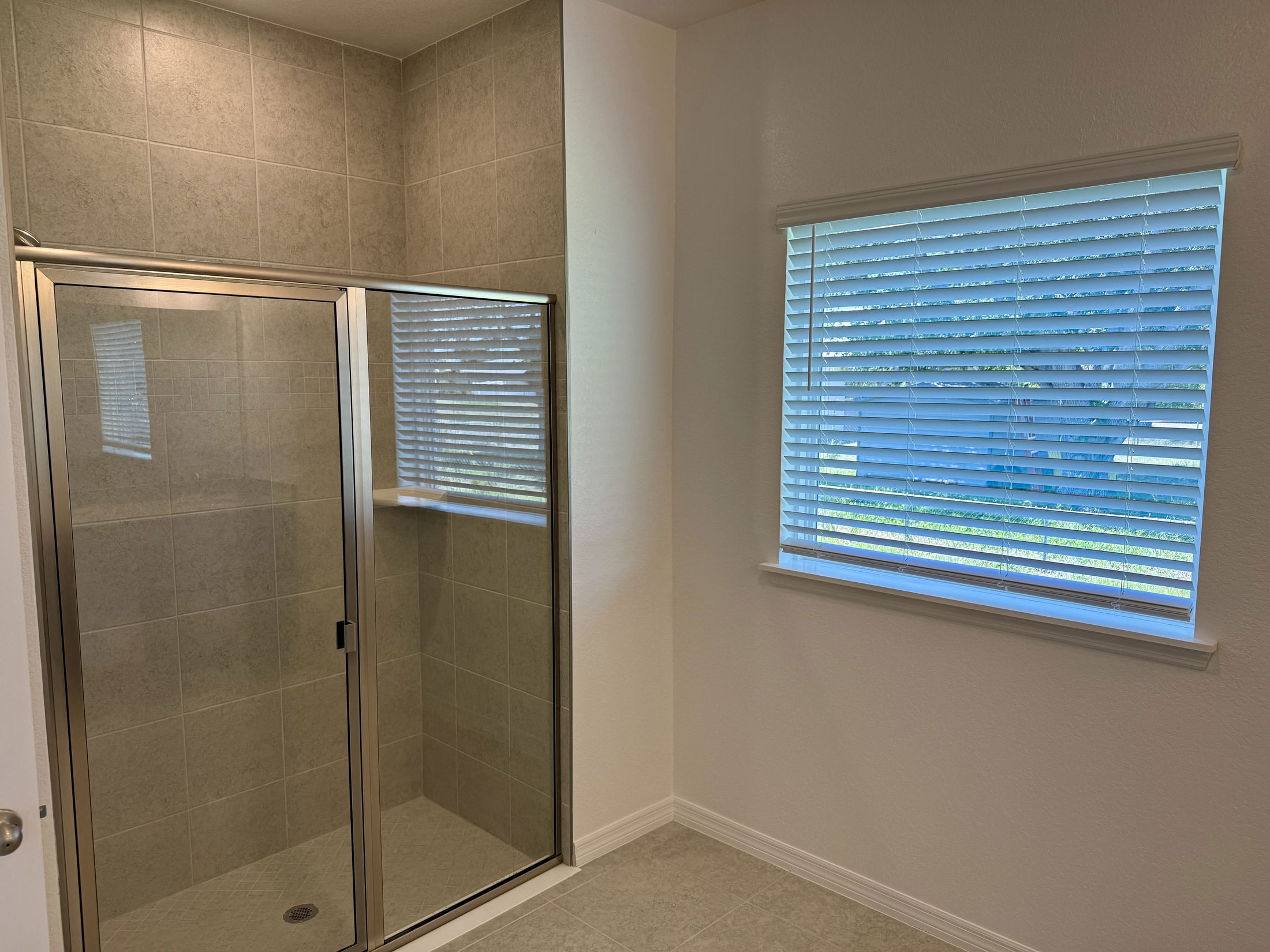 Modern bathroom with tiled shower enclosure and large window with blinds.