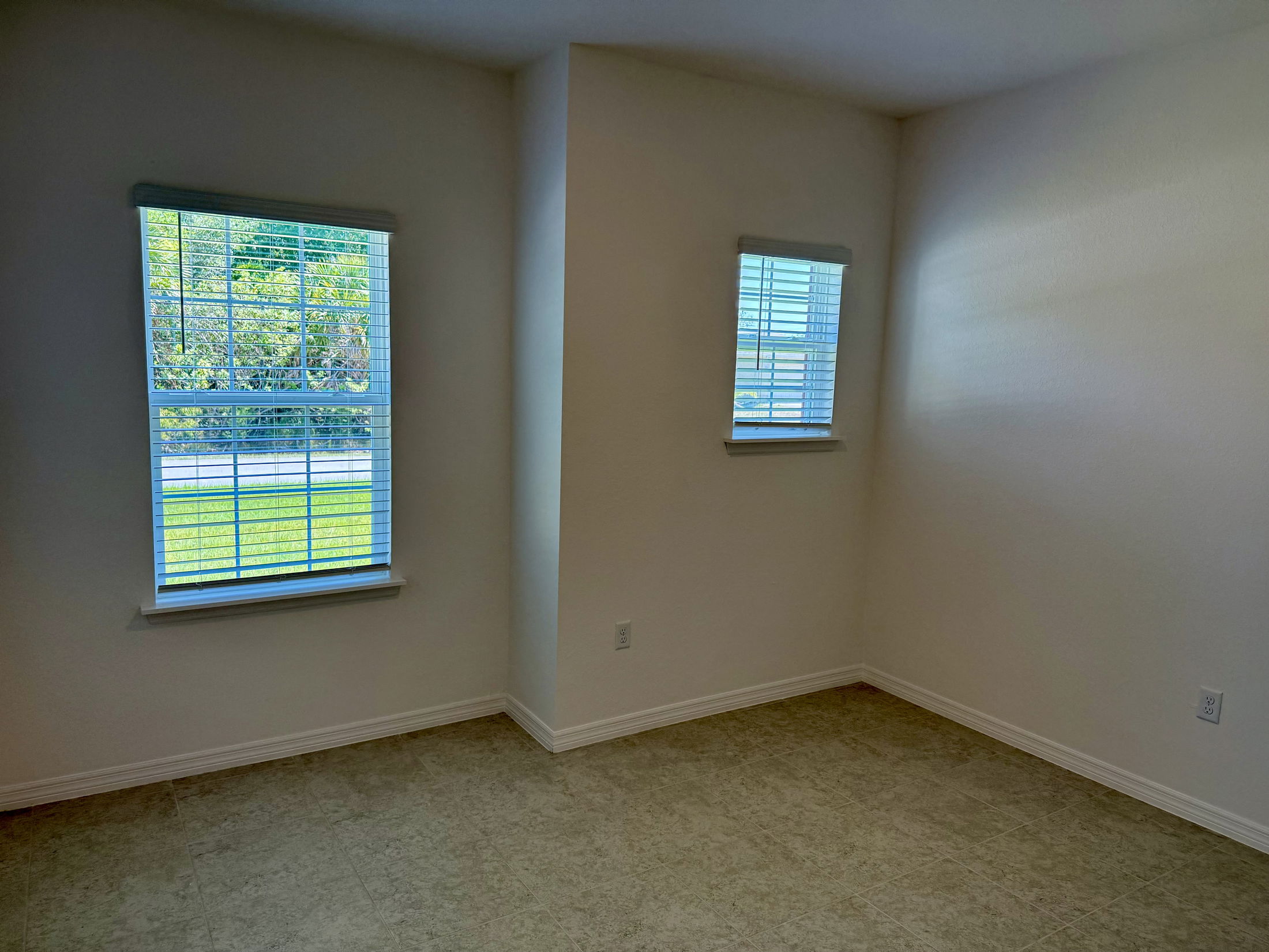Empty room with two windows and beige tile flooring, showcasing natural light and neutral walls.