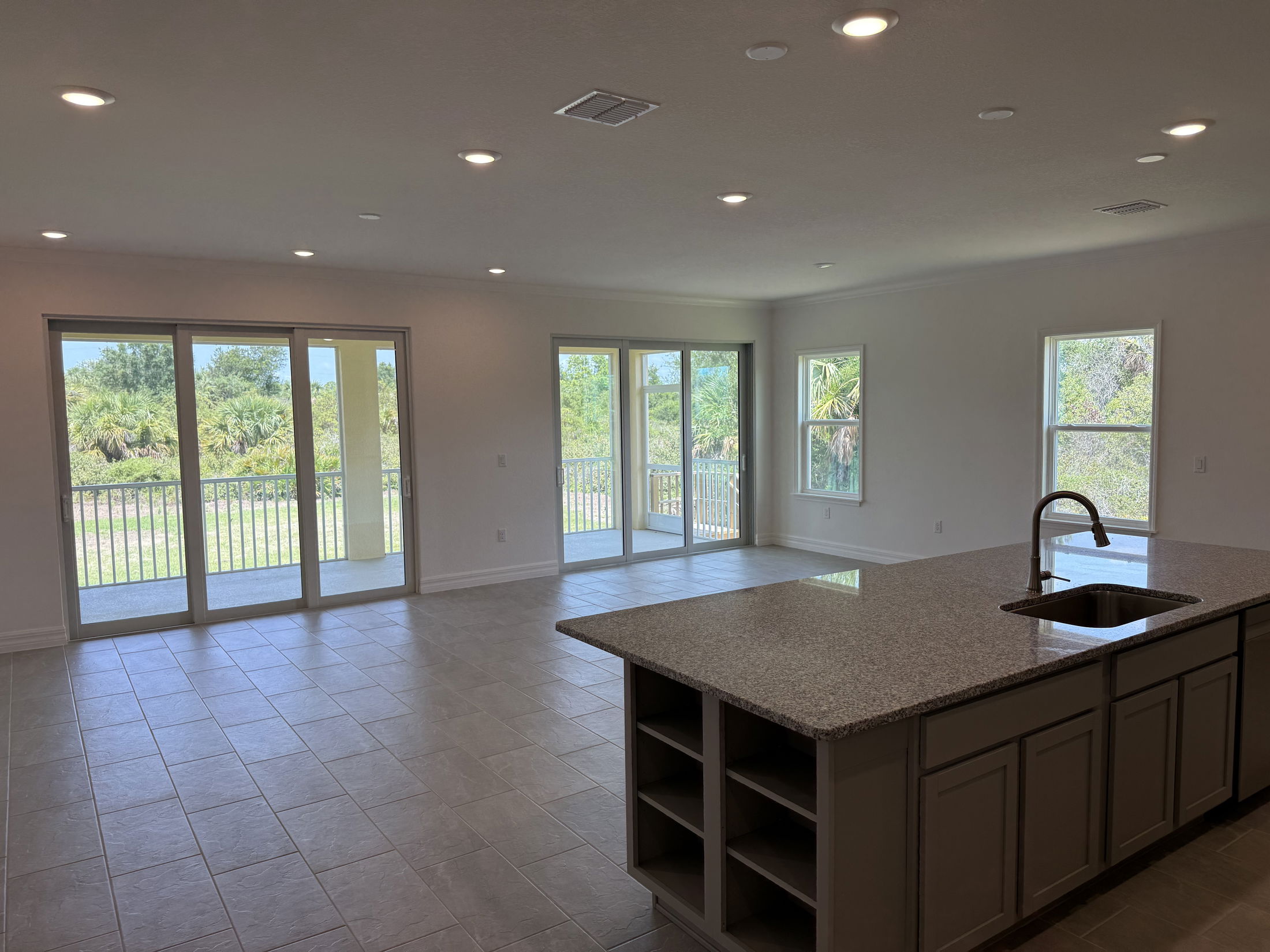 Spacious open-plan living area with large windows, sliding glass doors, and a modern kitchen island overlooking a lush outdoor view.