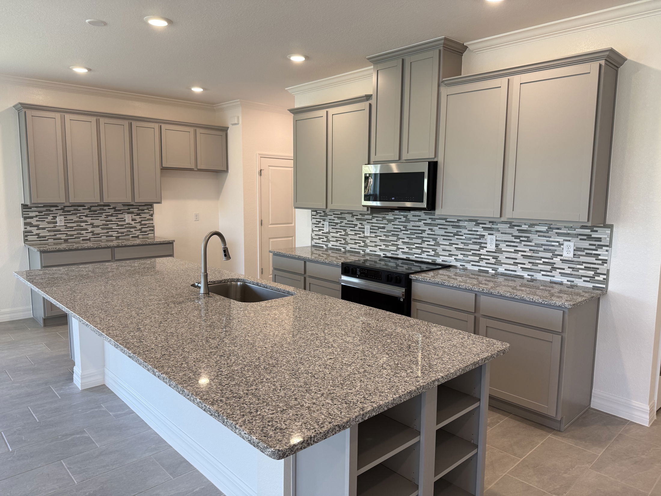 Modern kitchen interior featuring granite countertops, sleek gray cabinetry, and mosaic tile backsplash with stainless steel appliances.