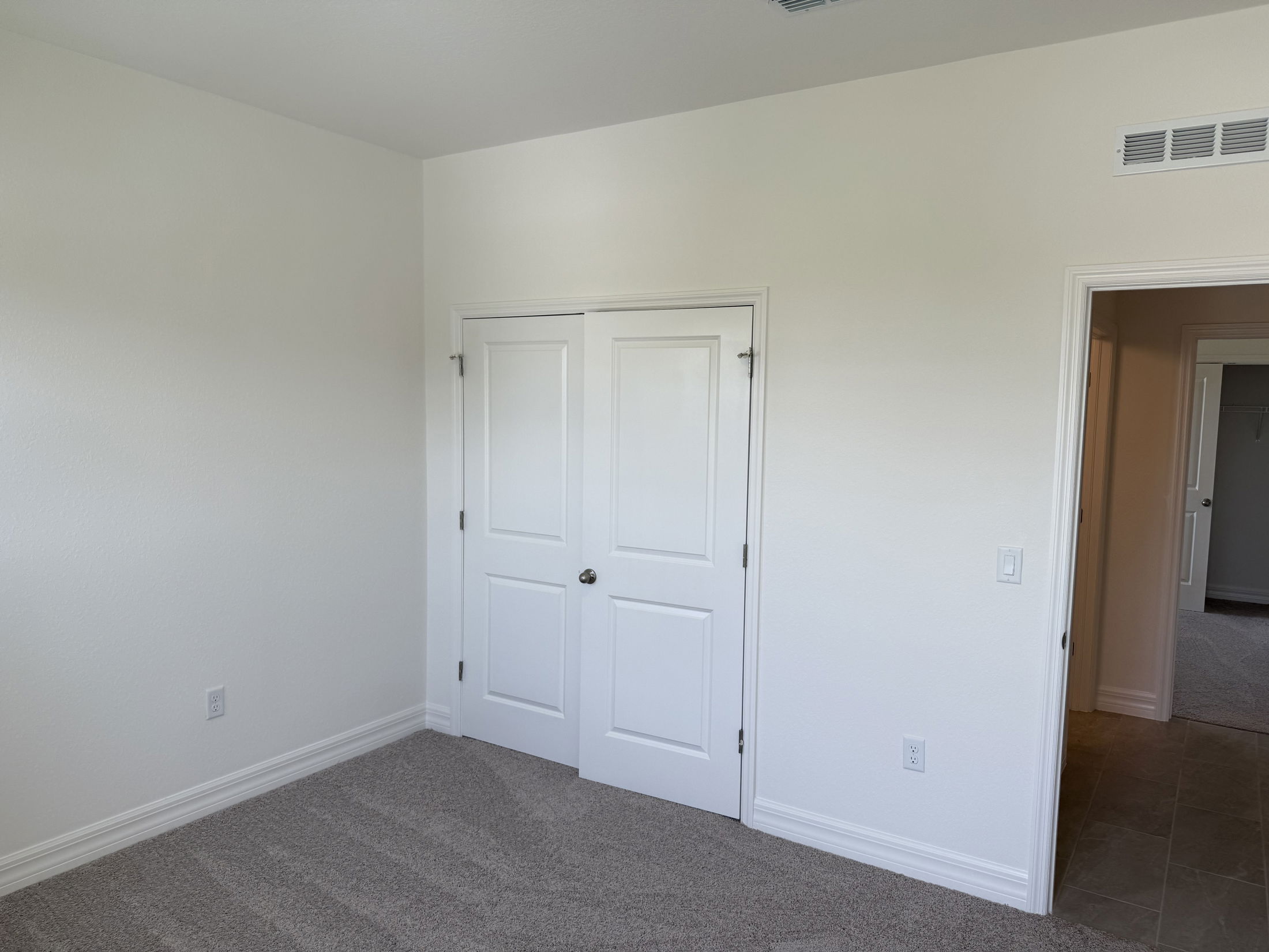 Empty white room with carpet flooring and a closed double door closet adjacent to an open doorway.