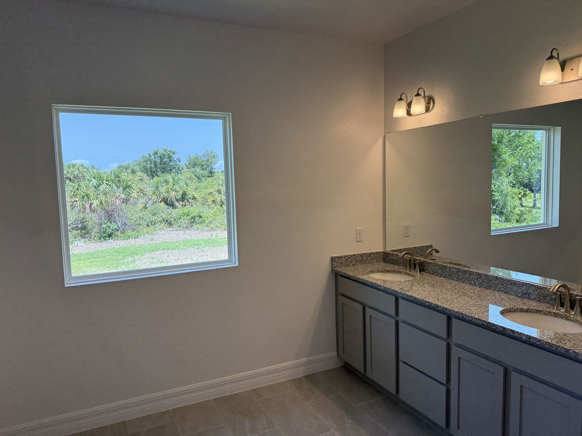 Modern bathroom with double sinks and granite countertop, featuring a large window overlooking lush greenery.