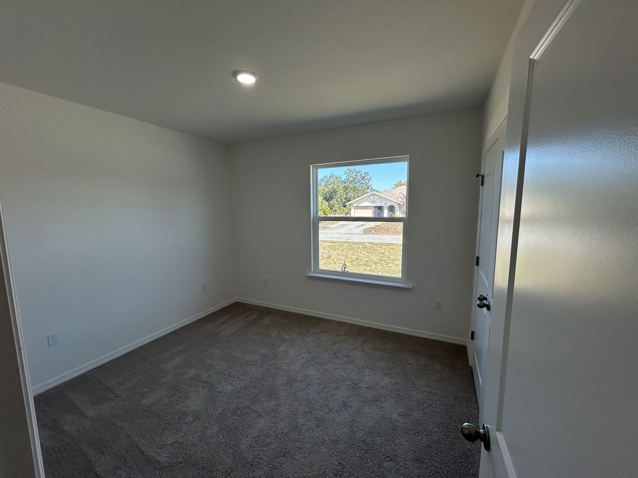Bright and spacious empty bedroom with carpet flooring, a window providing natural light, and a door leading outside.
