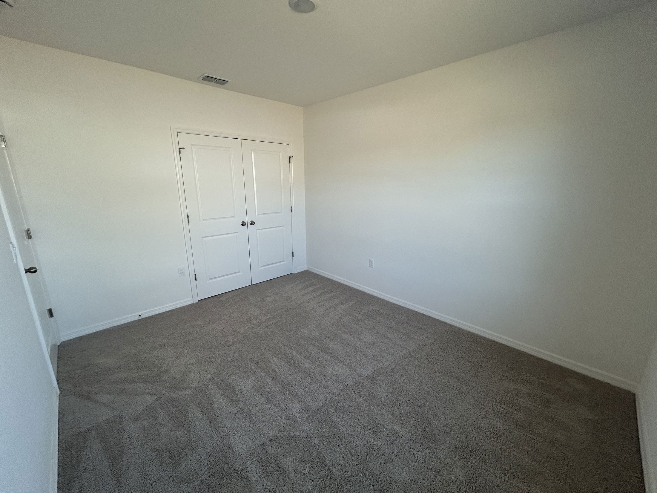 Empty bedroom with beige carpet and white walls featuring double doors.