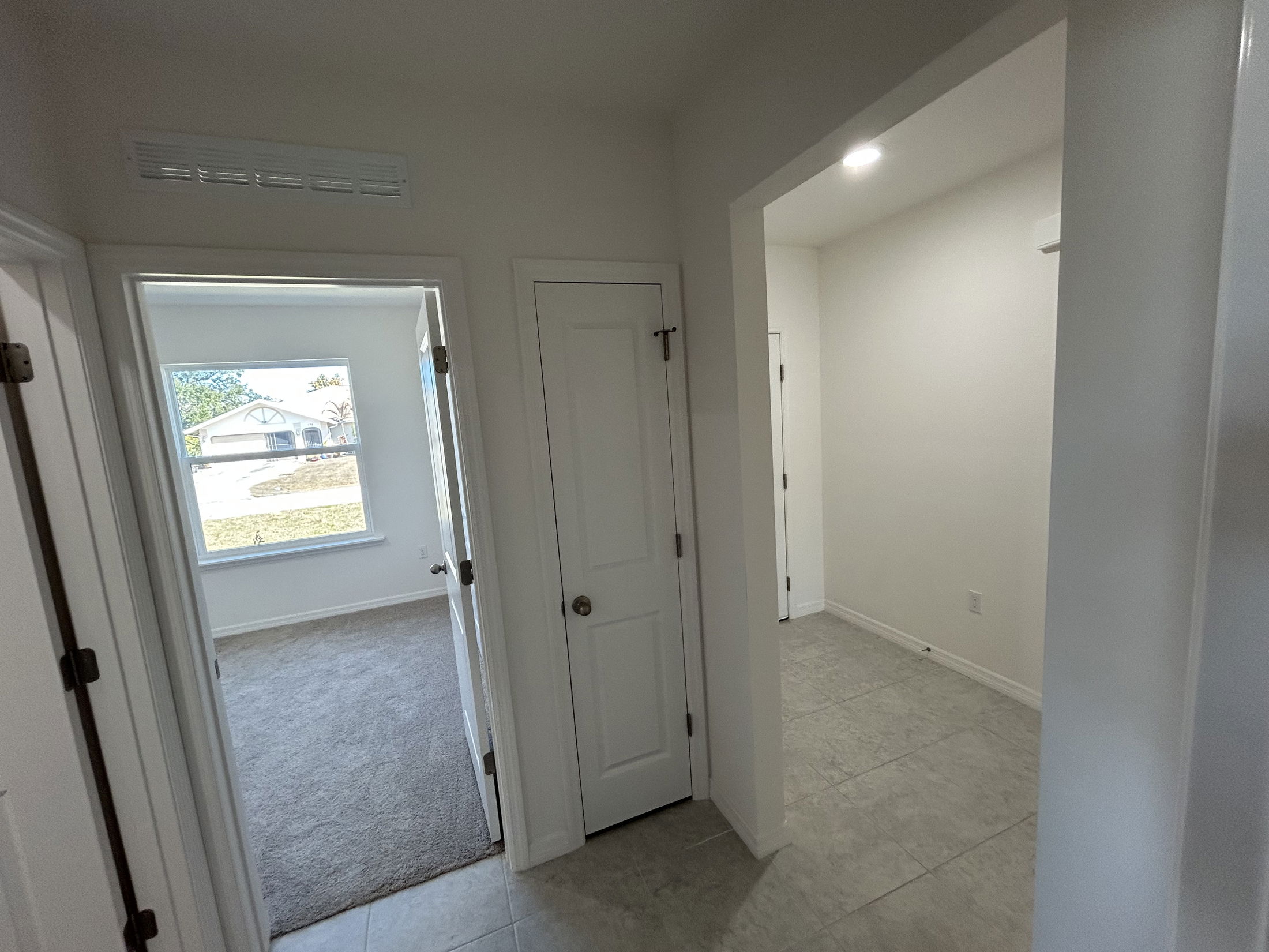 Interior hallway image featuring two doors, natural light from a window, and modern tile flooring.