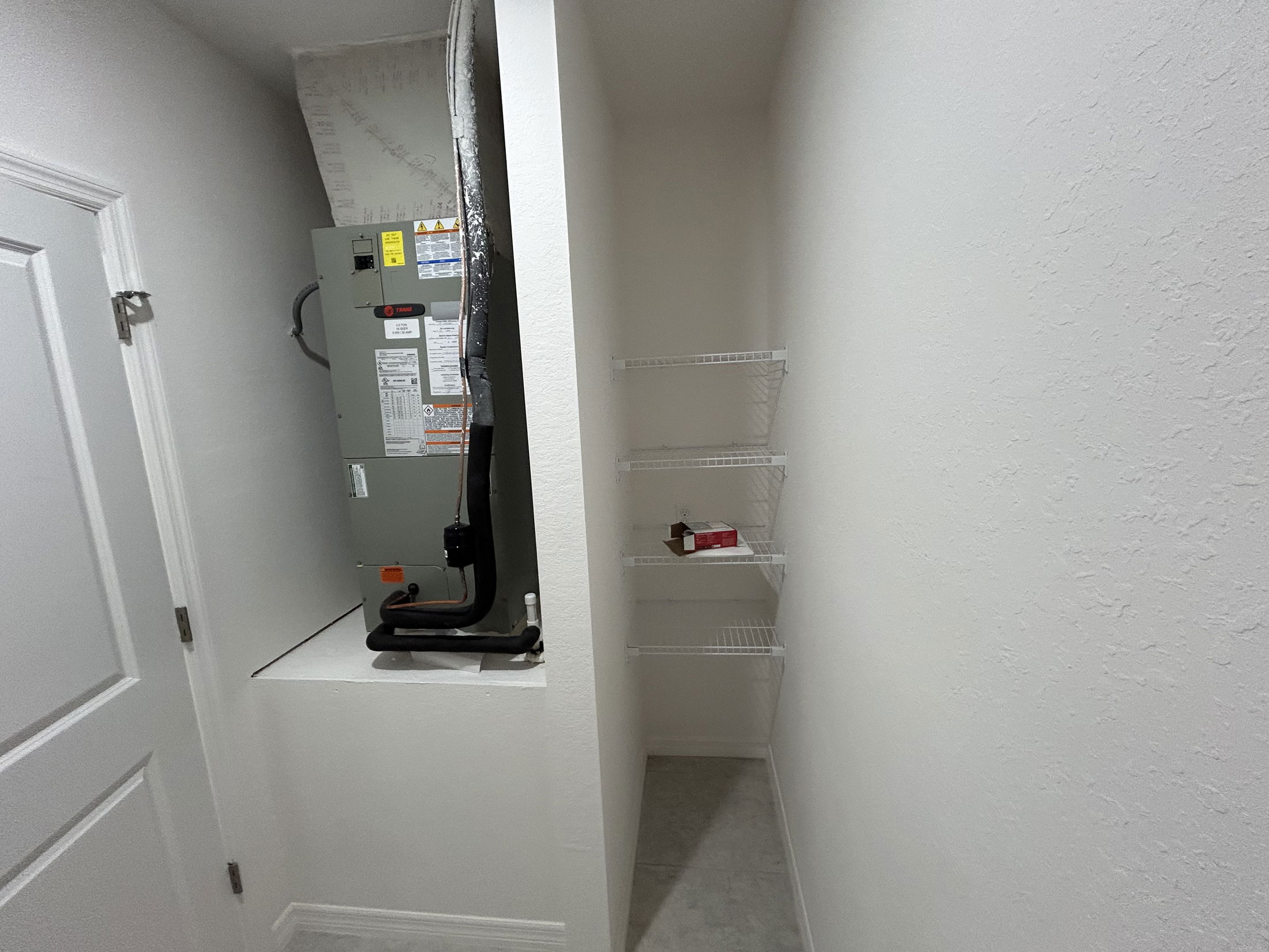 A small utility room featuring an HVAC unit and white wire shelving for storage.