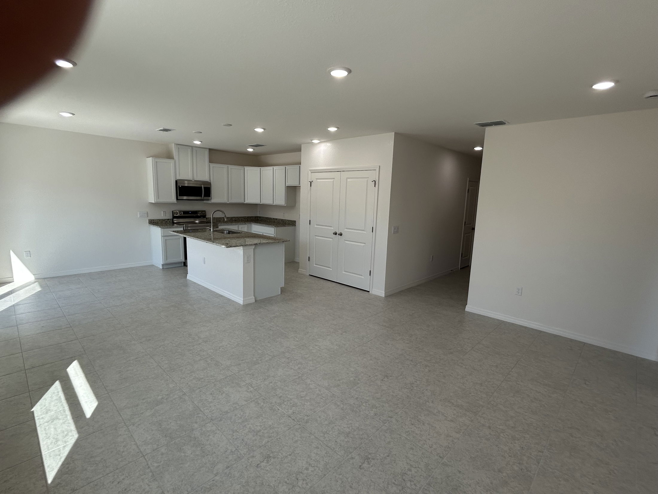 Spacious modern kitchen and living area with tile flooring and white cabinetry in a newly constructed home.
