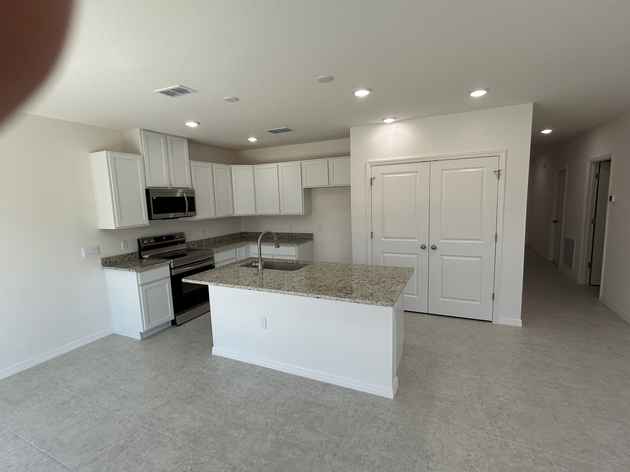 Spacious modern kitchen with white cabinetry, granite countertops, and stainless steel appliances in a newly built home.