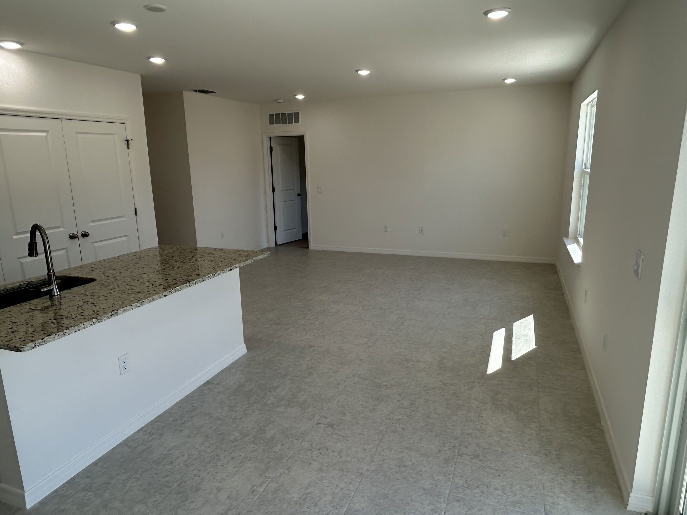 Spacious and modern open-concept living area with a granite kitchen island and natural lighting.