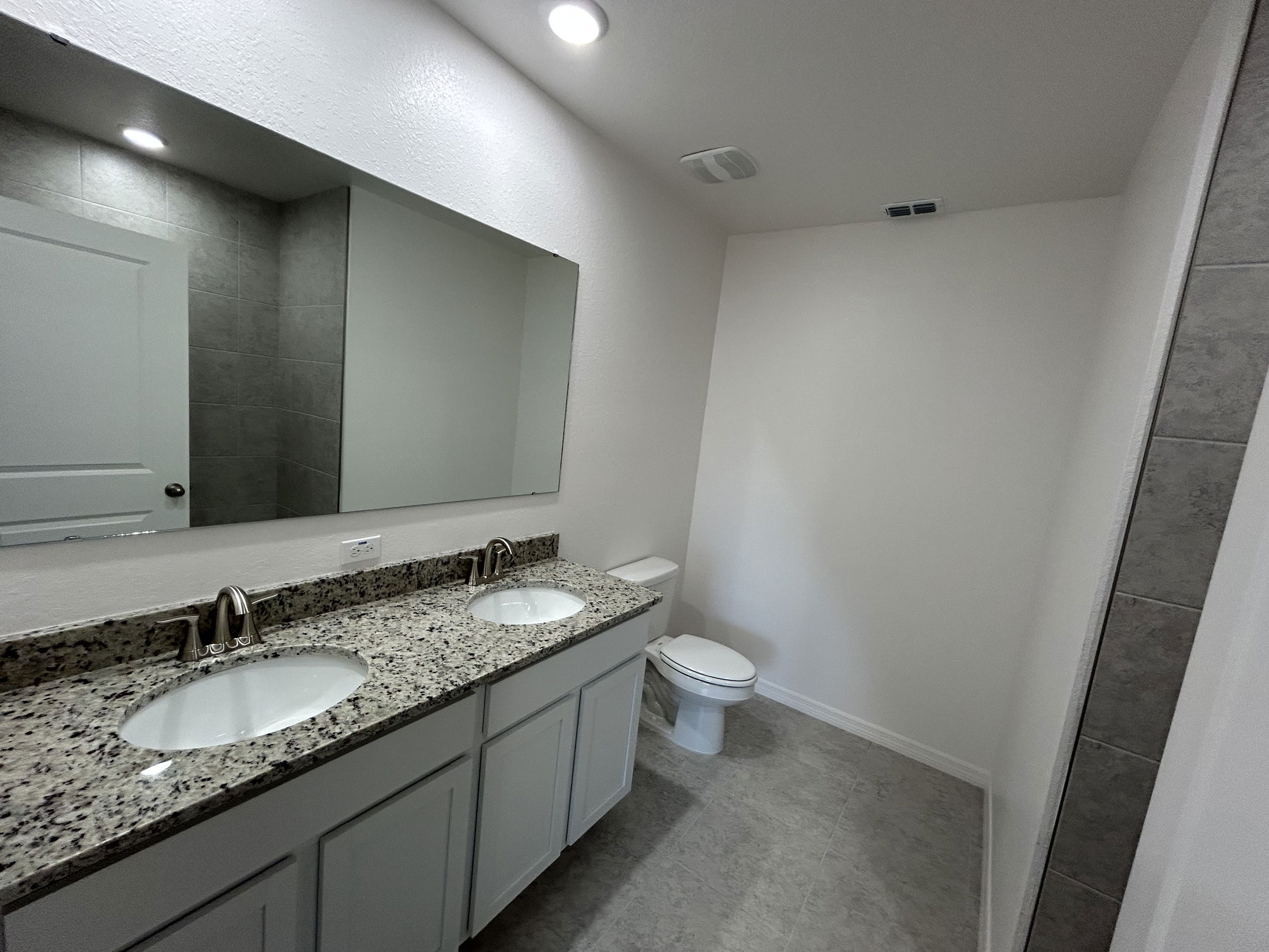 Spacious modern bathroom featuring double sinks, a large mirror, and neutral-colored tiles.