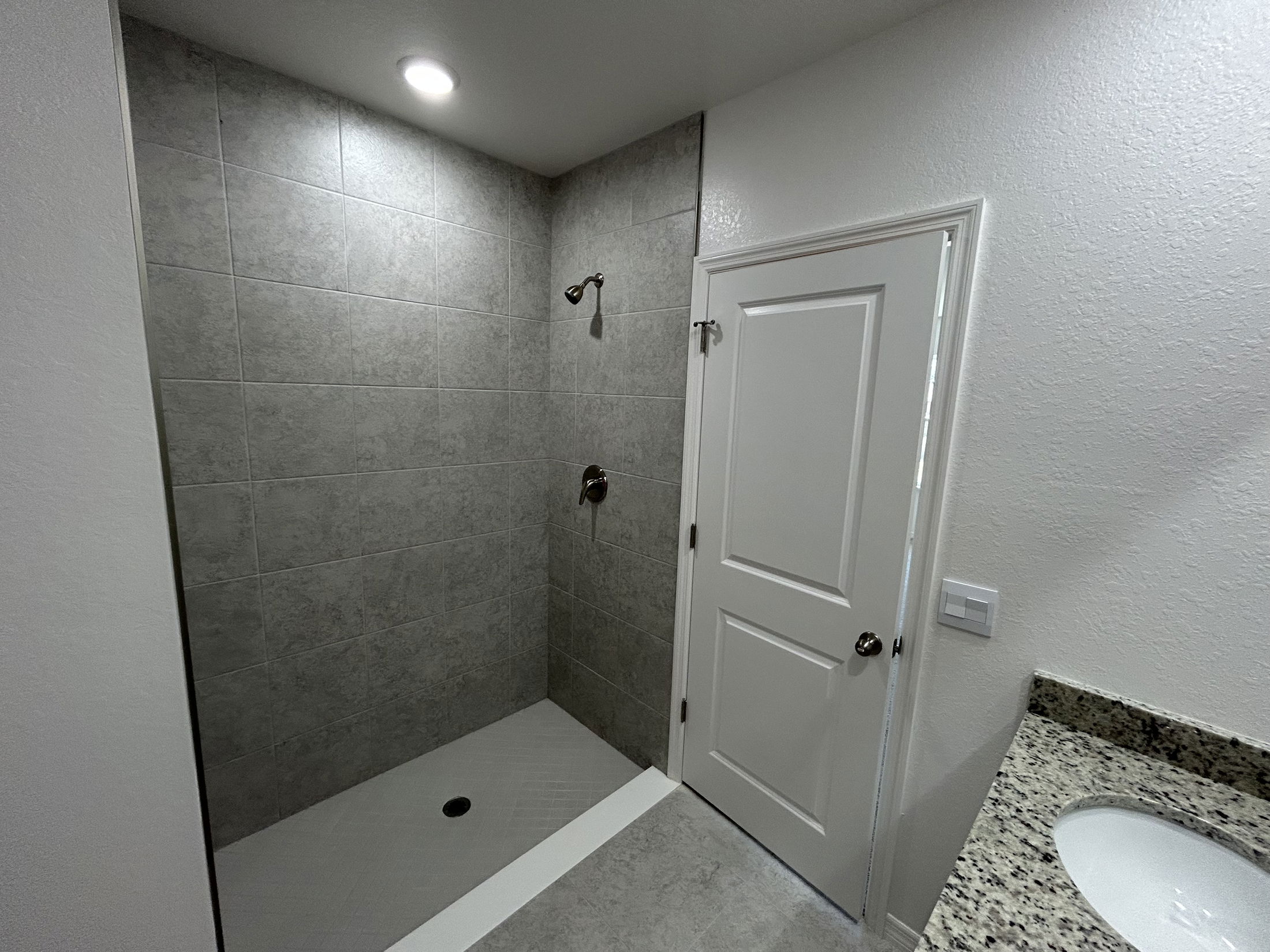 Modern bathroom with a spacious tiled shower, granite countertop, and light-colored walls.