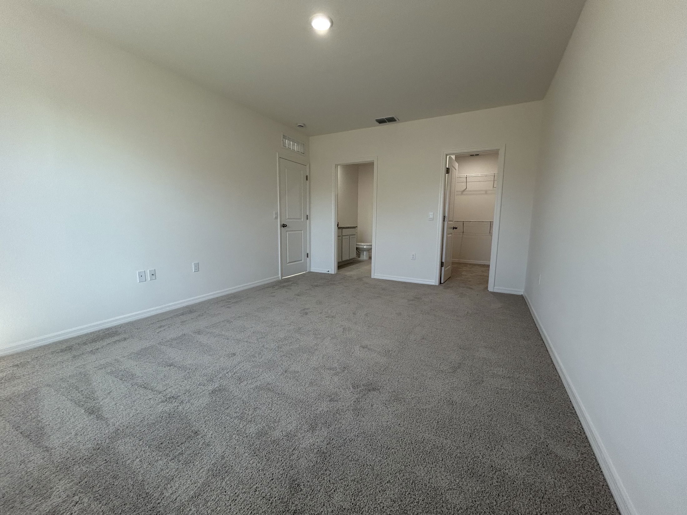 Spacious, empty room featuring beige carpet and white walls with a doorway leading to a bathroom and closet.