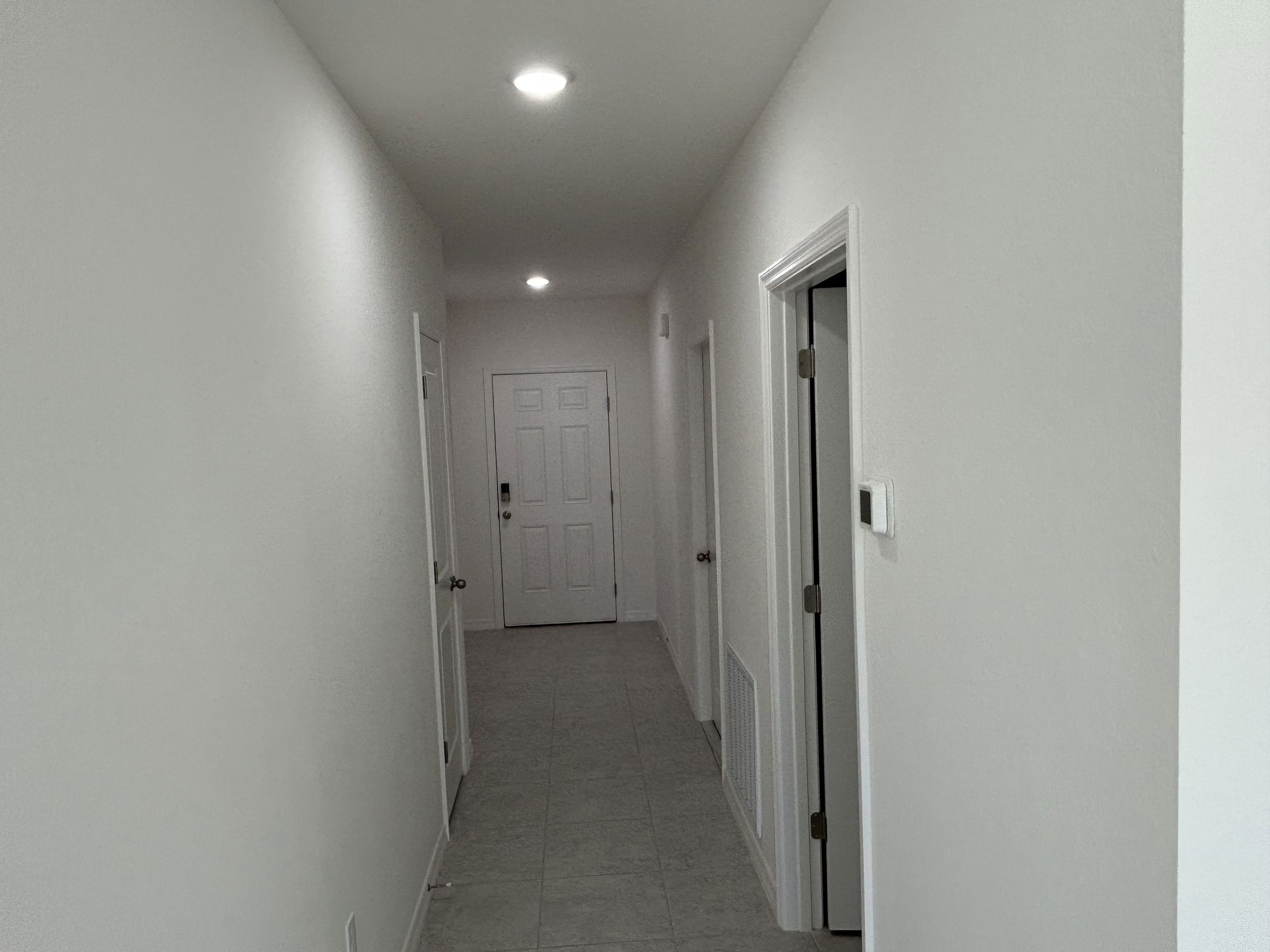 Modern hallway interior with white walls, ceiling lights, and doors leading to different rooms.