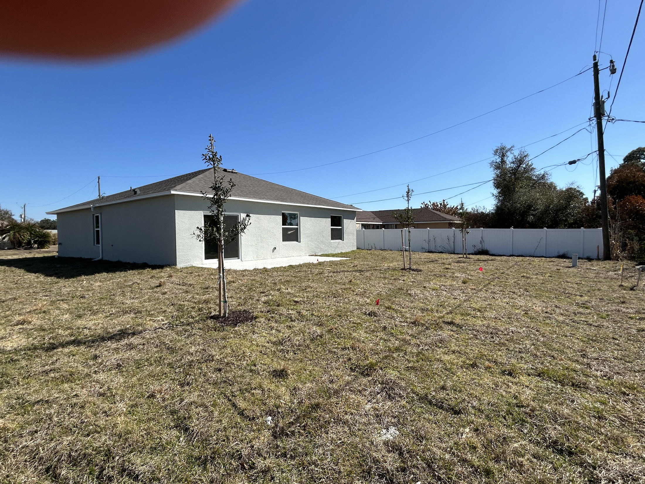 Single-story house with a grassy yard and trees under a clear blue sky.