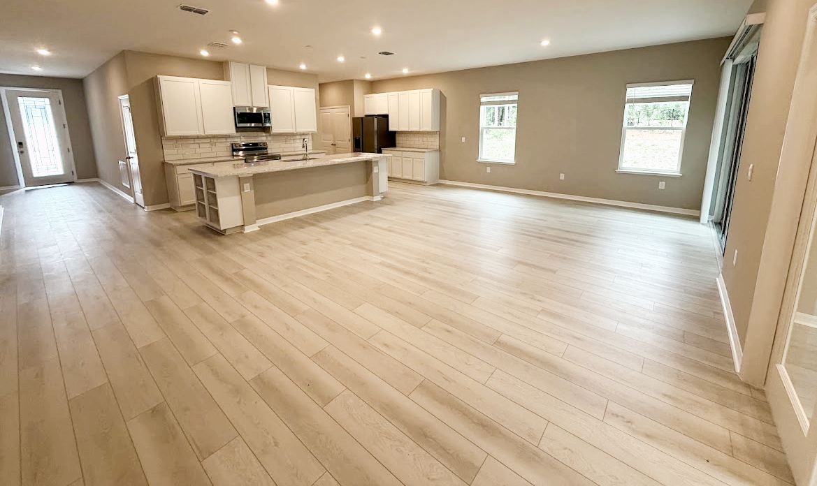 Spacious light-filled living area with wood flooring and modern kitchen countertops.