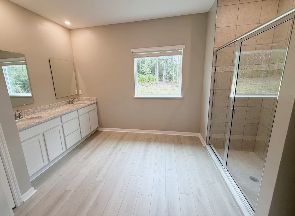 Spacious bathroom featuring a double vanity, large mirror, and a glass shower enclosure.