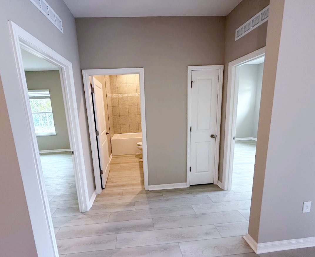 A spacious room with light-colored walls and tiled flooring, featuring doorways leading to adjacent rooms and a bathroom.