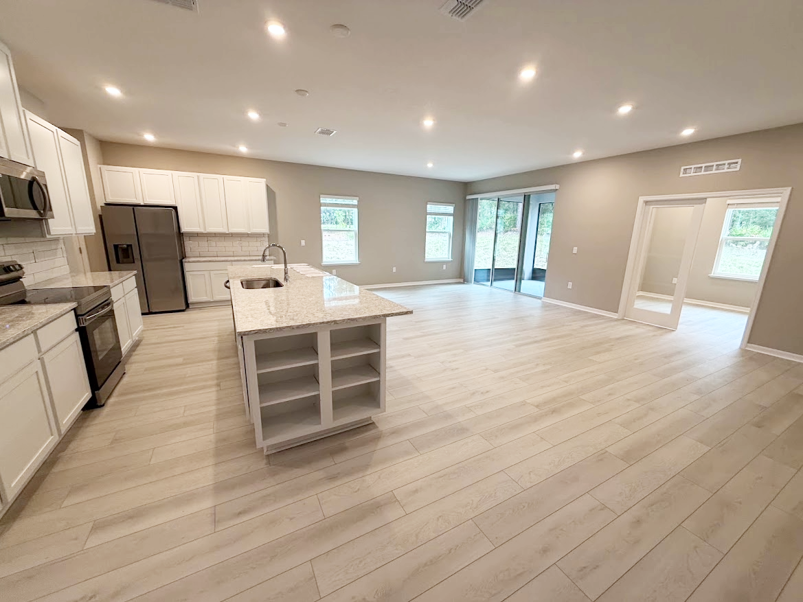 Spacious modern kitchen and living area with light-colored cabinetry and large windows.