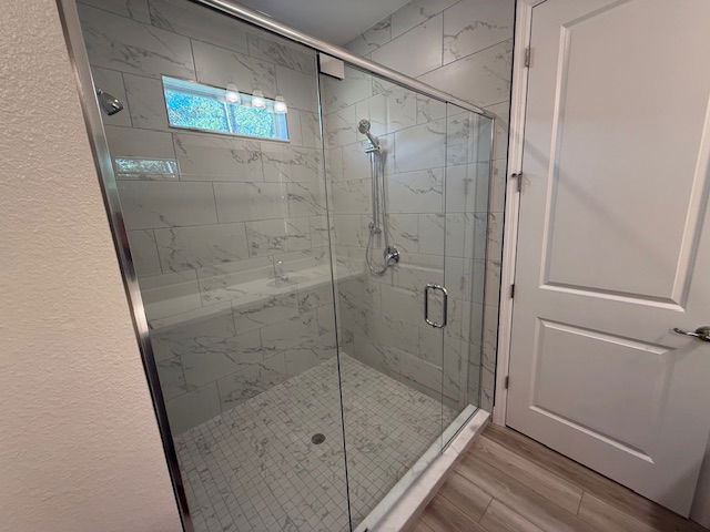 A modern bathroom features a glass-enclosed shower with marble-style tiles and a sliding door.