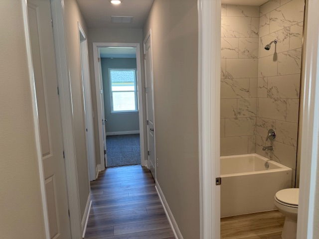 Hallway leading to a bedroom with natural light, featuring a modern bathroom with marble tile and a bathtub on the right.