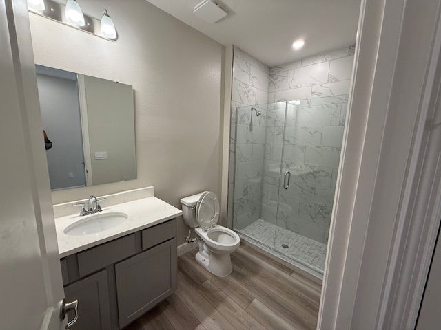 Modern bathroom with a glass-enclosed shower, marble-tiled walls, wooden flooring, and a gray vanity.