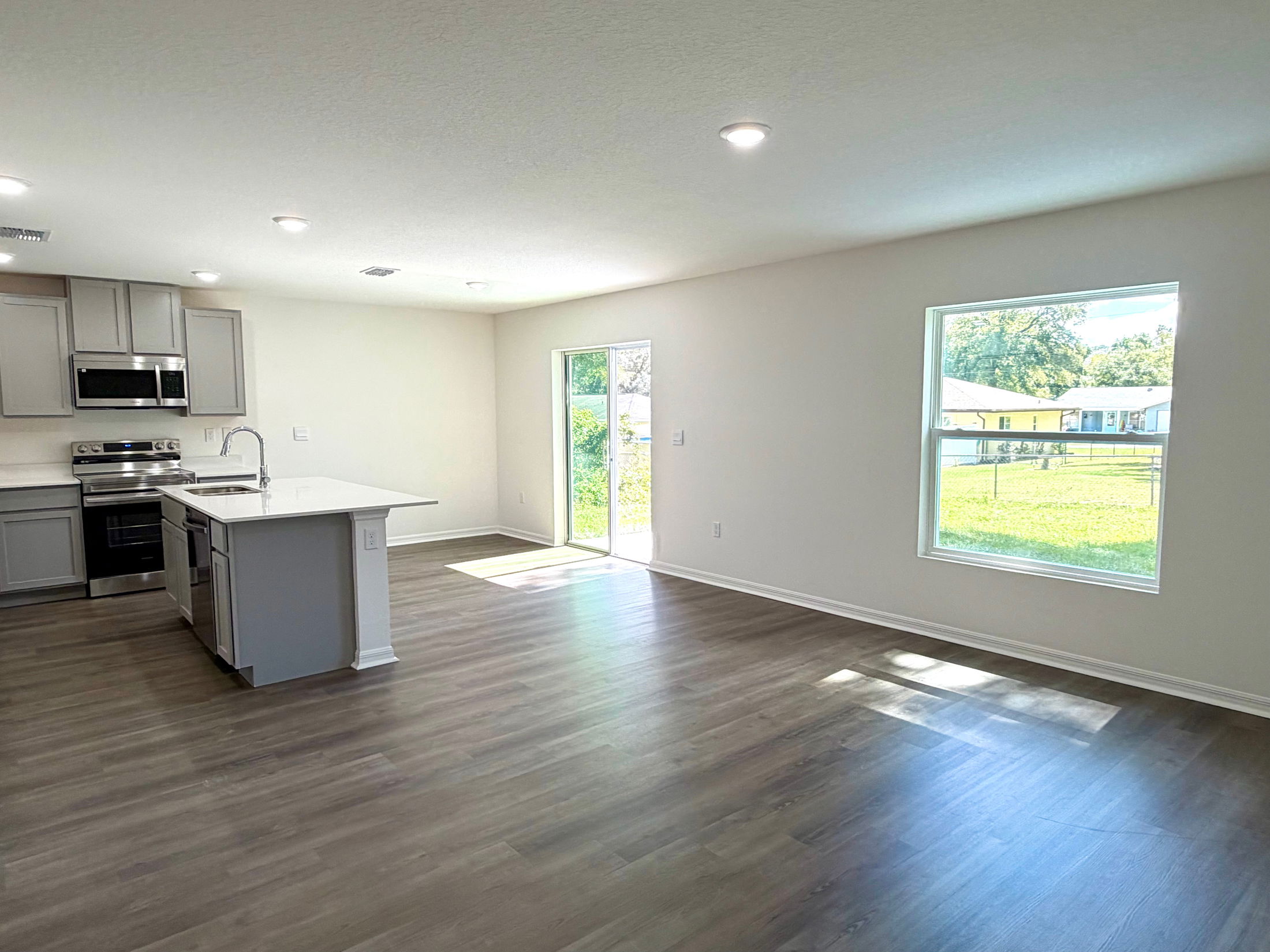 Modern open-concept kitchen and living area with hardwood floors and large windows.
