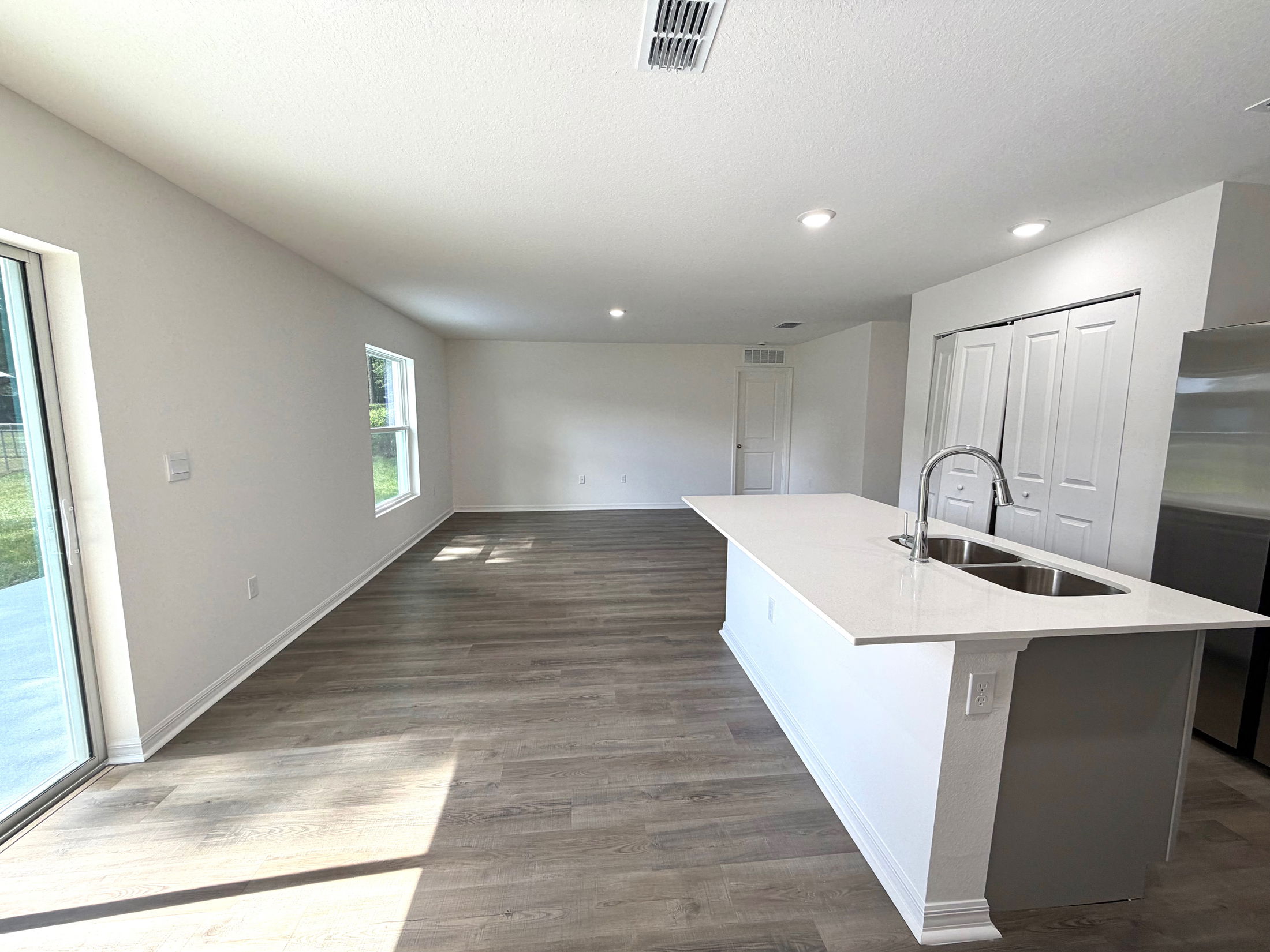 Spacious open-concept kitchen and living area with sleek wooden flooring, white countertops, and abundant natural light.