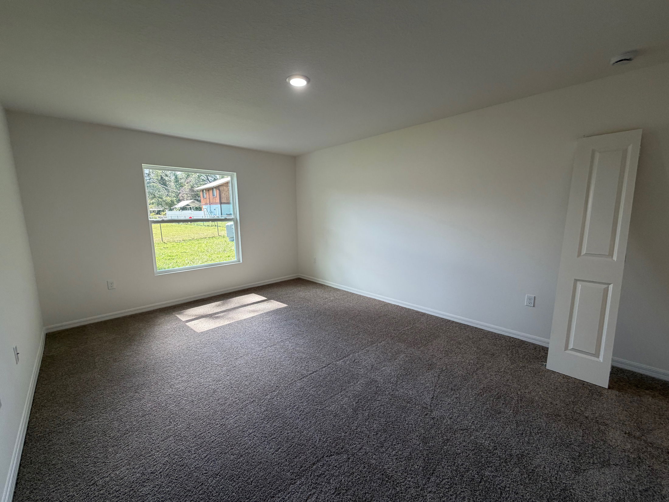 Empty room with beige carpet, natural light from a window, and a leaning door against the wall.