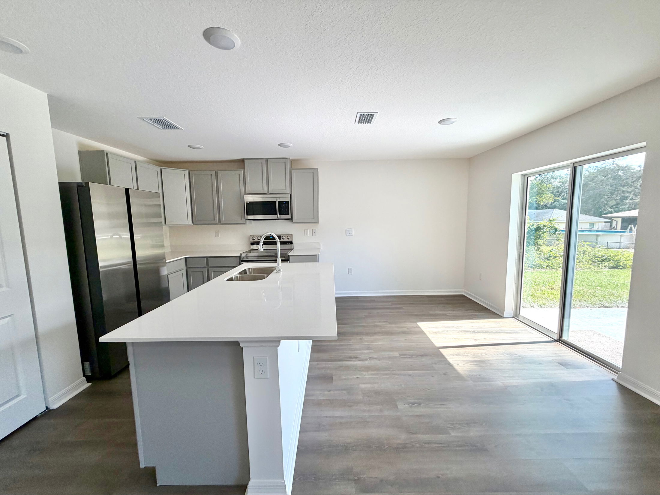 Modern kitchen with gray cabinets, stainless steel appliances, and a large island counter, featuring sliding glass doors leading to a backyard.
