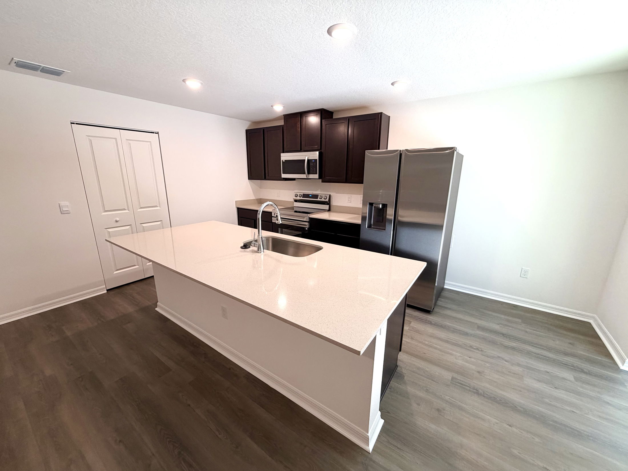 Modern kitchen with dark wood cabinets, stainless steel appliances, and a spacious island featuring a sink and quartz countertop.