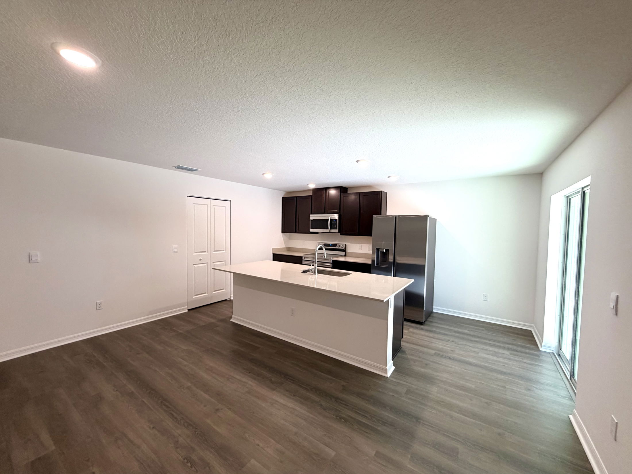 Modern kitchen featuring dark wood cabinets, stainless steel appliances, and a spacious layout with a large island and vinyl flooring.