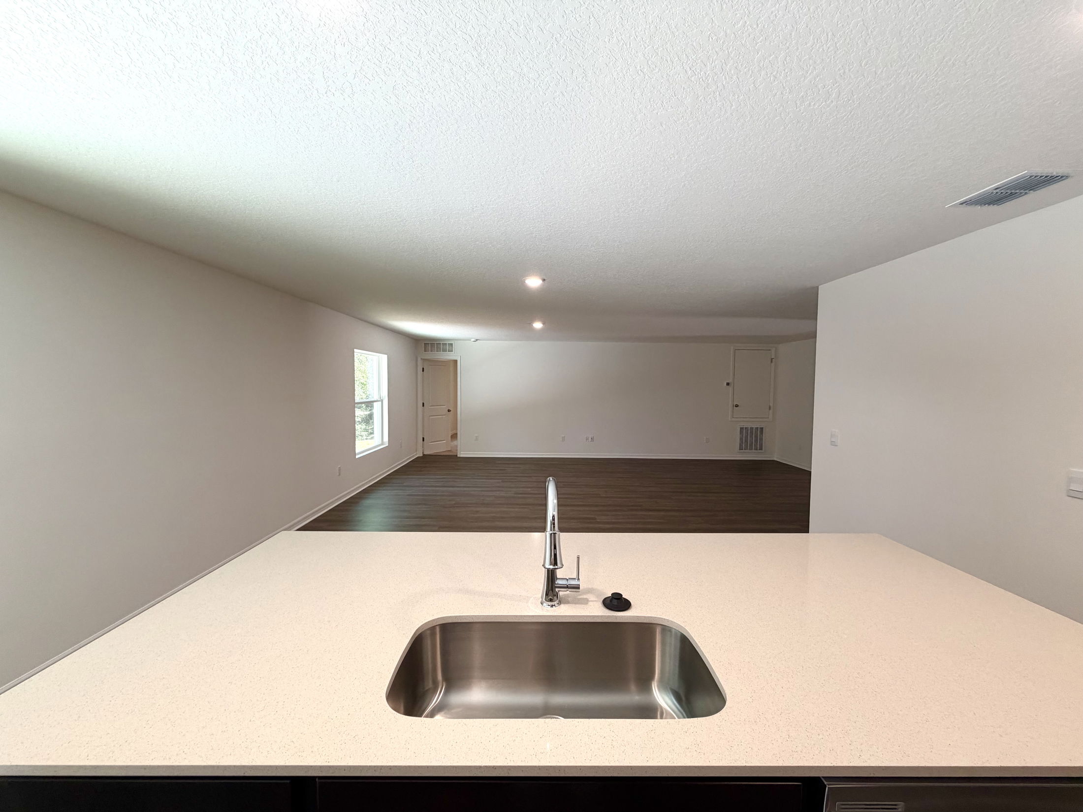 Modern kitchen view featuring a sleek countertop with a stainless steel sink overlooking an open living space with wooden flooring.